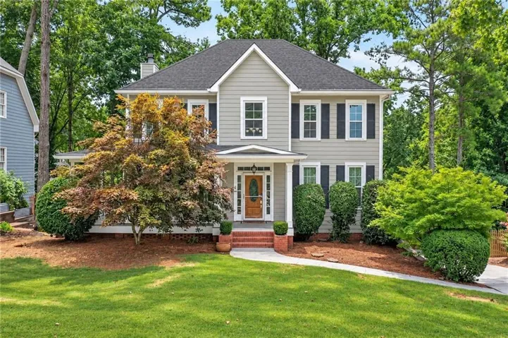 Two-story residence featuring light gray siding, dark shutters, and a prominent front entry with a wood-finish door
