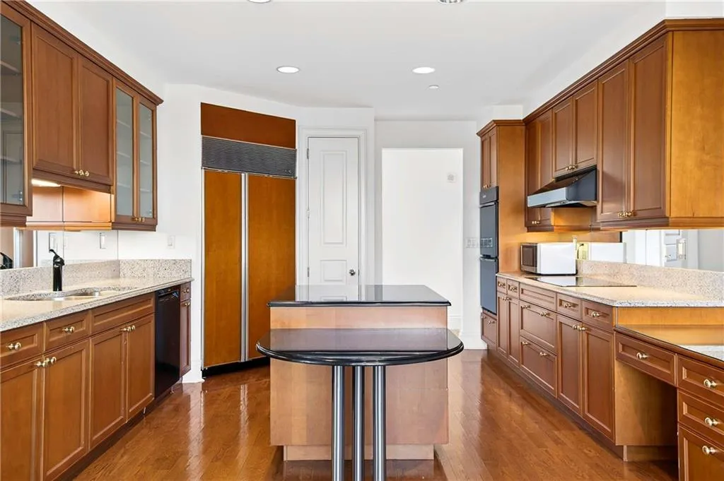 Kitchen featuring glass fronted cabinets, a kitchen island, wood finish cabinets, dark stone counters, and recessed lighting