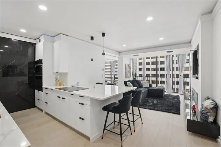 Open-concept living area with light wood-finish flooring, white cabinetry, a kitchen island with seating, a built-in oven, and floor-to-ceiling windows