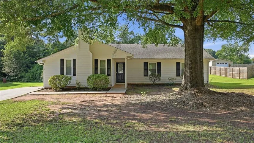 White siding ranch home featuring a prominent mature tree, paved driveway, and established landscaping