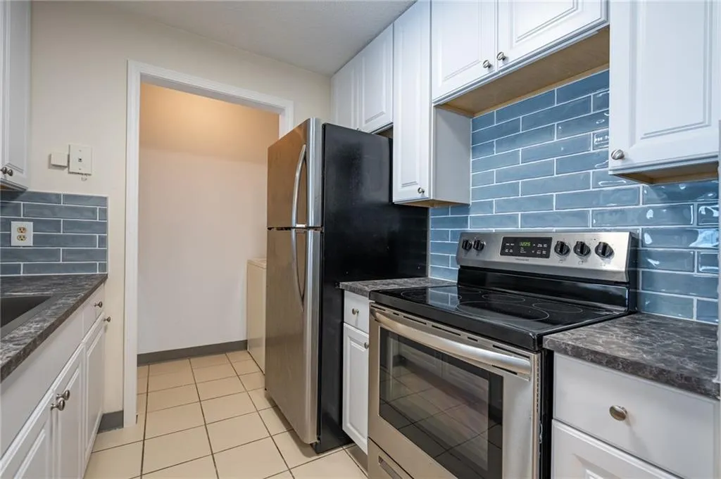 Kitchen with stainless steel appliances, white cabinets, light tile patterned floors, backsplash, and baseboards