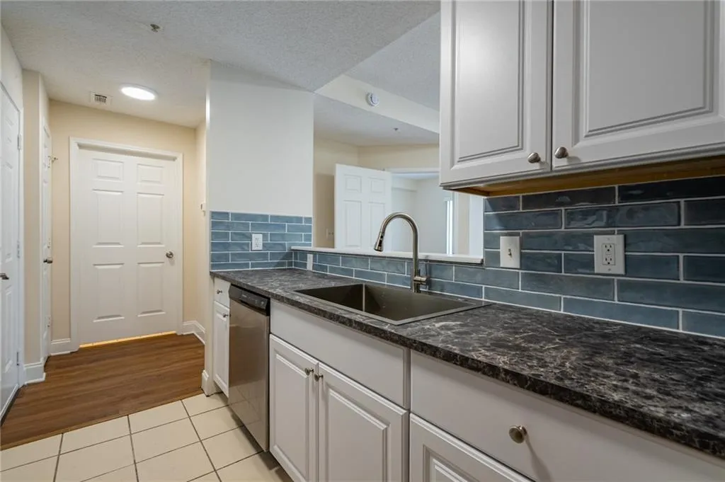 Kitchen with a sink, stainless steel dishwasher, light tile patterned floors, tasteful backsplash, and white cabinets