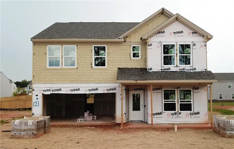 Two-story home with a two-car garage, multiple windows, a covered front porch, and partial siding