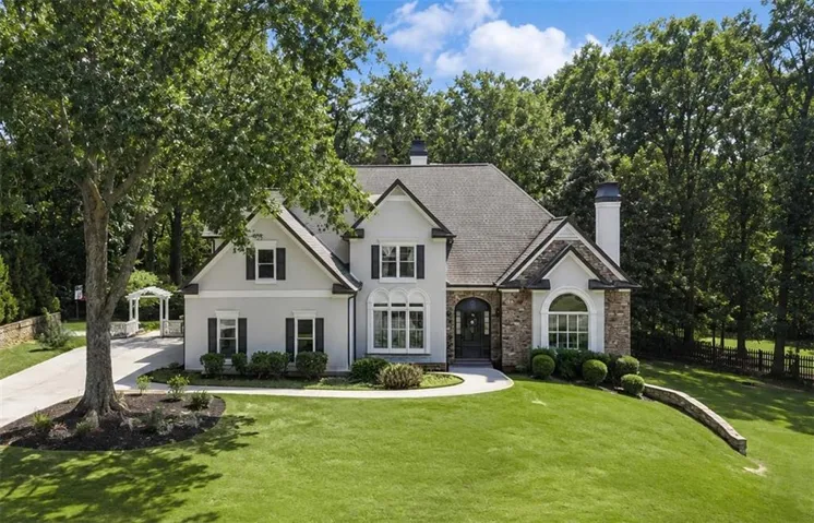 Stucco and stone exterior featuring a dark asphalt shingle roof, arched entryway, and dark-paneled window shutters