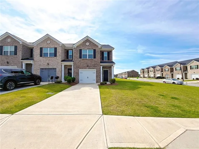 Brick exterior with dark shutters, white garage doors, and concrete driveways