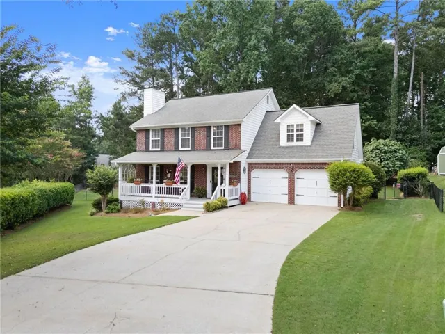 Traditional brick and siding exterior featuring a covered front porch with white railings, a two-car garage with white doors, a gabled roofline, and a paved driveway