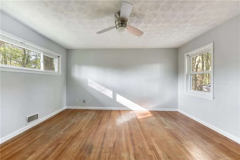Empty room featuring ceiling fan, a textured ceiling, a healthy amount of sunlight, and hardwood / wood-style floors