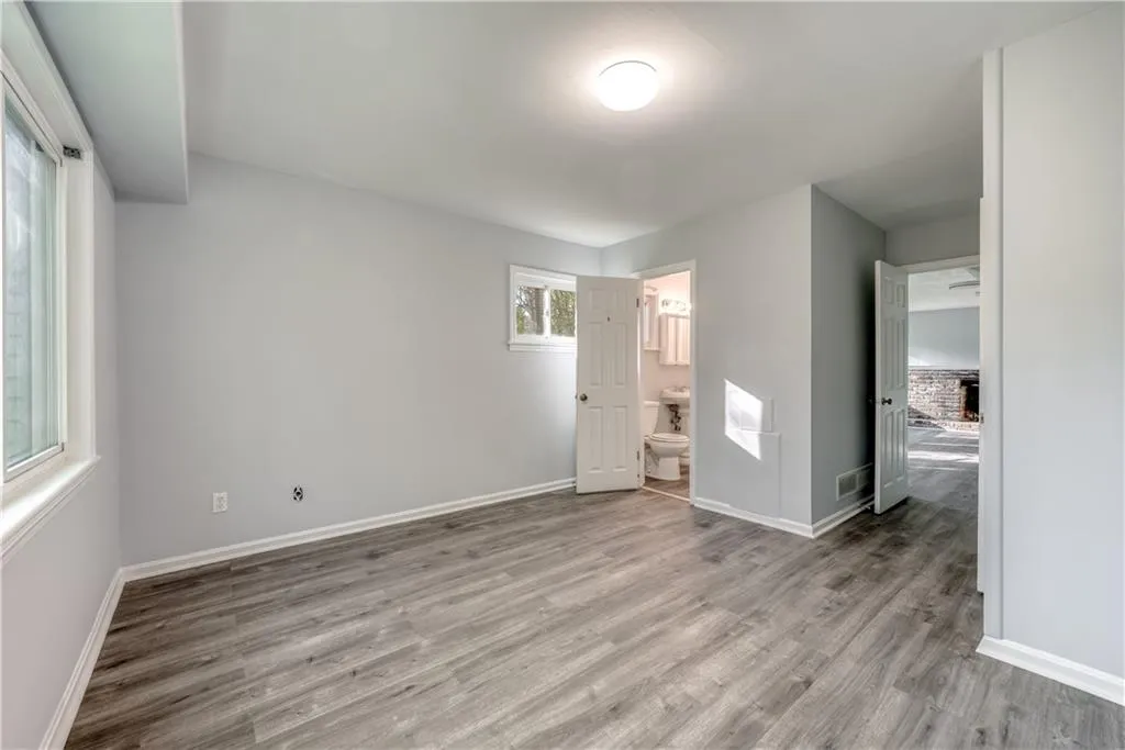 Unfurnished bedroom featuring a brick fireplace, ensuite bath, and light hardwood / wood-style flooring