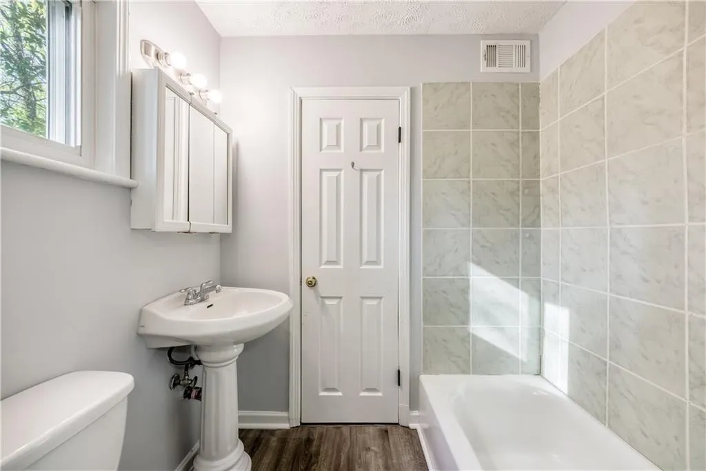 Bathroom featuring toilet, a textured ceiling, wood-type flooring, and tiled shower / bath