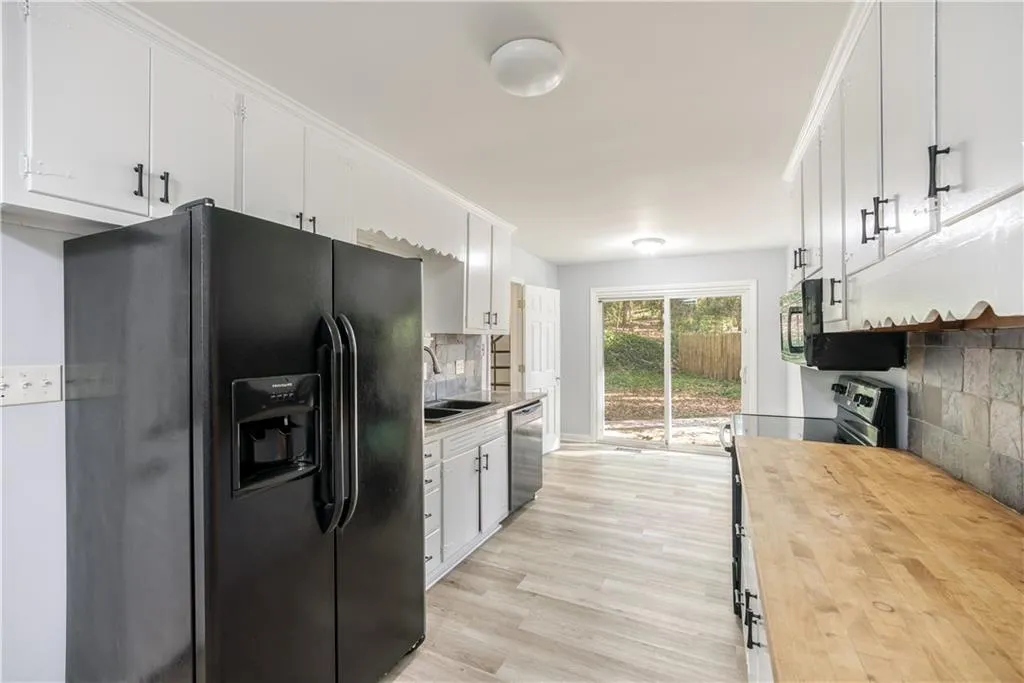 Kitchen with sink, white cabinets, light hardwood / wood-style flooring, butcher block countertops, and black appliances
