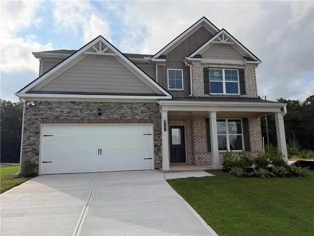 Two-story residence featuring a brick and stone facade, covered front porch with pillars, and a two-car garage with decorative hardware