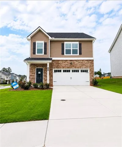Two-story brick and siding home featuring a two-car garage with white paneled doors, manicured front lawn, concrete driveway, and gable roofline with architectural detailing