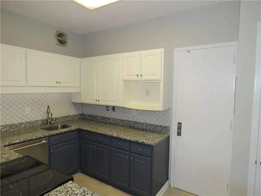 Corner kitchen featuring a stainless steel sink with a high-arc faucet, granite-style countertops, white upper cabinetry, and contrasting dark lower cabinetry
