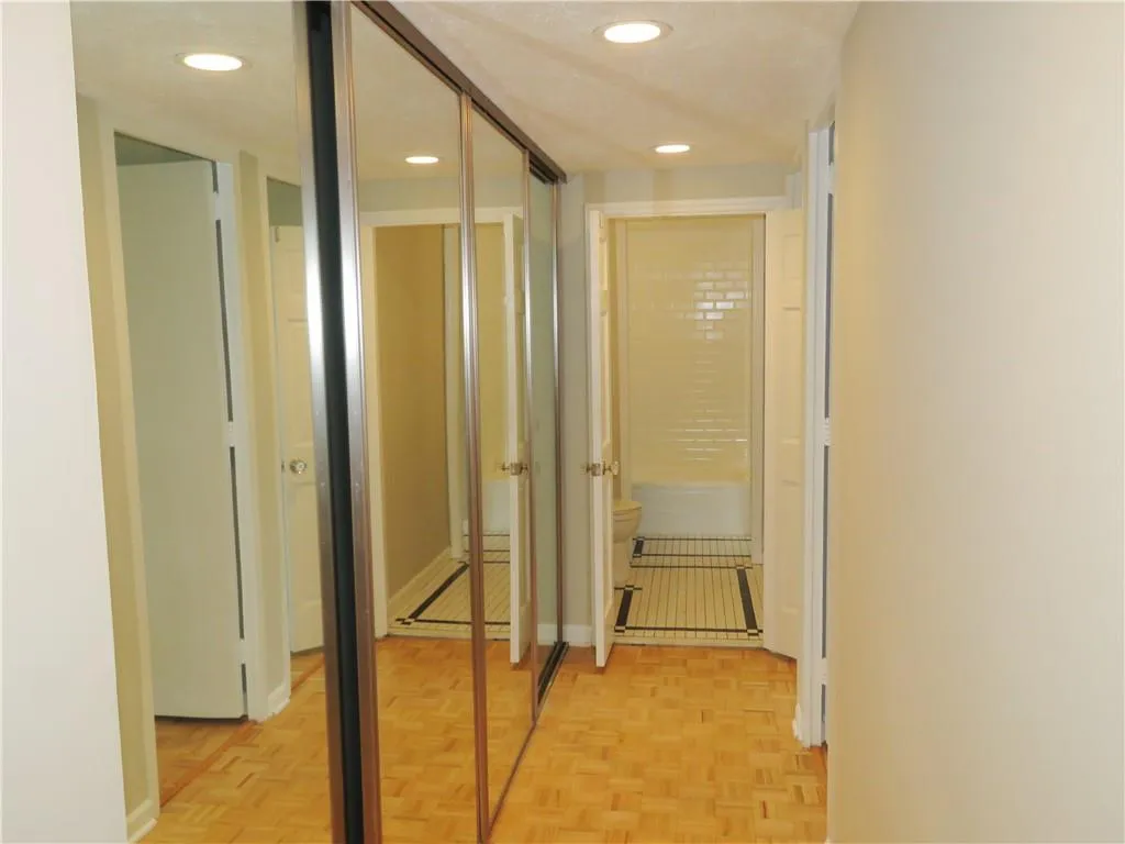 Spacious hallway featuring mirrored closet doors with brushed metal frames, warm wood-finish flooring, recessed ceiling lighting, and multiple doorways providing access to adjoining rooms