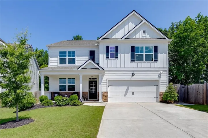 White siding exterior with black shutters, covered front porch, attached garage, concrete driveway, and landscaped front yard