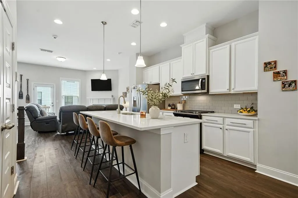 Kitchen with white cabinets, a breakfast bar, a kitchen island with sink, open floor plan, and pendant lighting