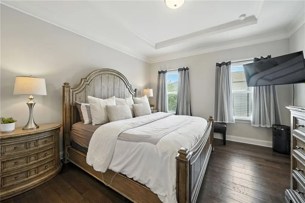 Bedroom with dark wood finished floors, a tray ceiling, and crown molding