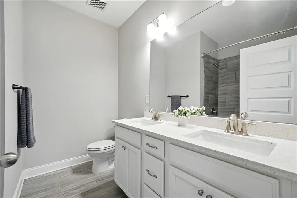 Full bath with double vanity, tiled shower, and wood tiled floors