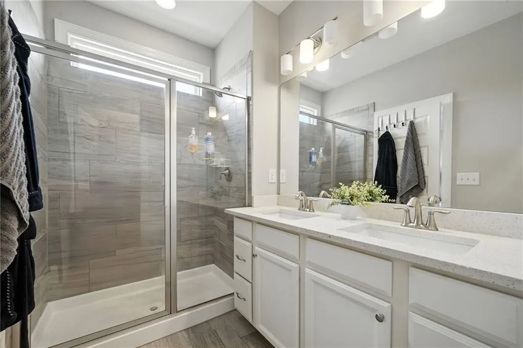 Full bath with a shower stall, double vanity, and light wood-style flooring