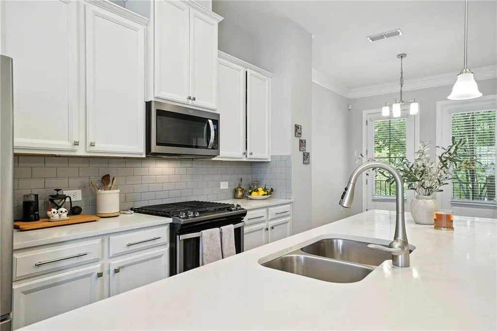Kitchen with appliances with stainless steel finishes, white cabinetry, decorative backsplash, light stone countertops, and hanging light fixtures