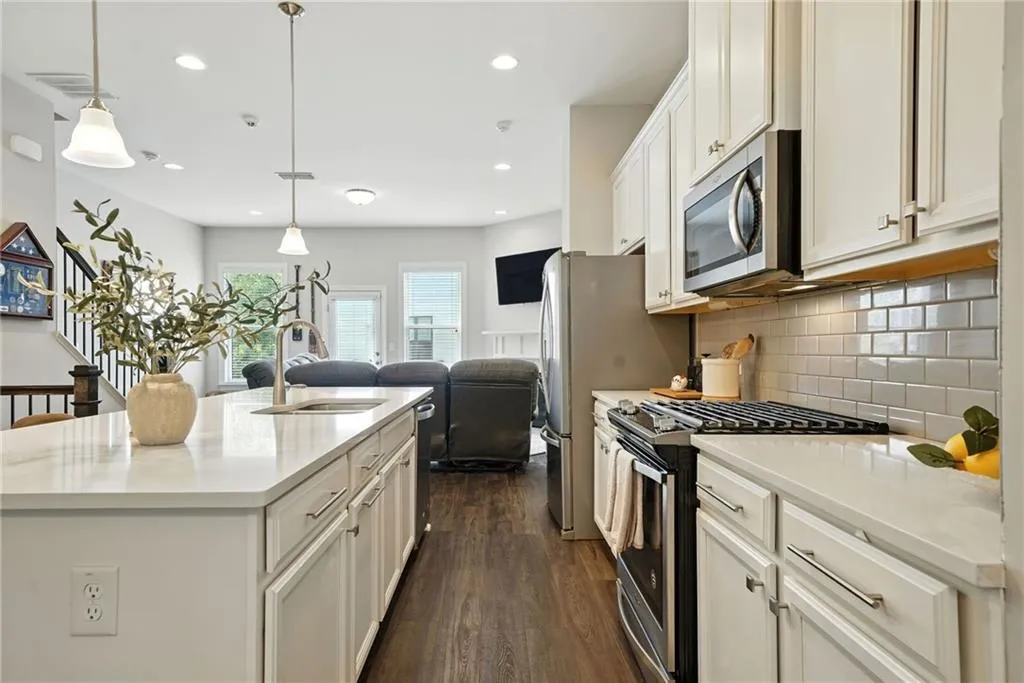 Kitchen featuring appliances with stainless steel finishes, decorative backsplash, white cabinetry, dark wood-style flooring, and hanging light fixtures