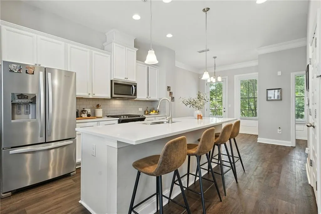 Kitchen with stainless steel appliances, an island with sink, white cabinetry, dark wood-style floors, and decorative light fixtures
