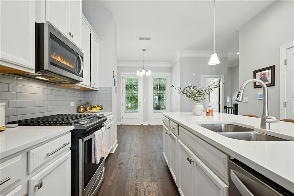 Kitchen with appliances with stainless steel finishes, white cabinetry, light stone counters, ornamental molding, and decorative light fixtures