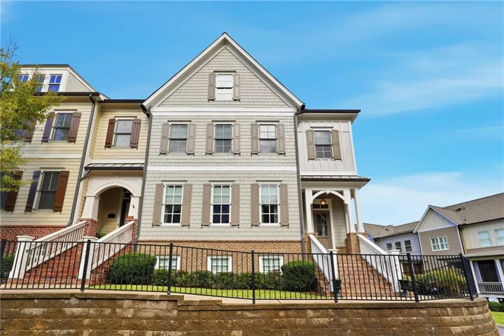 Multi-story townhome with light-colored siding, dark shutters, an arched entryway, and a covered porch