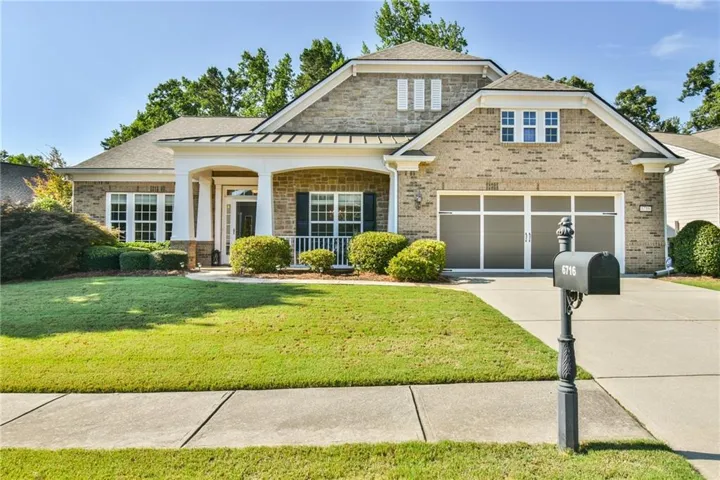 Brick exterior featuring a covered entry porch, white columns, two-car garage, and a lush front lawn with mature landscaping