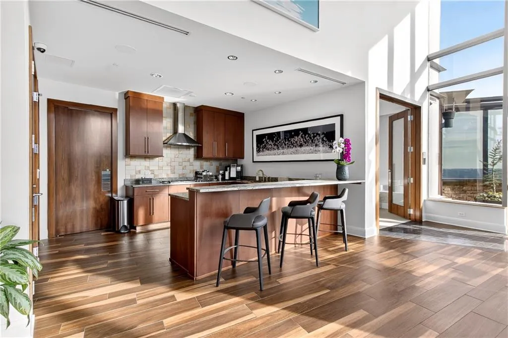 Kitchen featuring a breakfast bar area, dark wood finished floors, a peninsula, wall chimney range hood, and brown cabinets