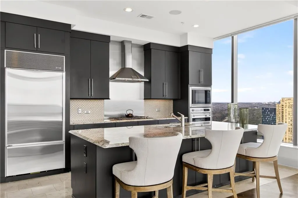 Kitchen with dark cabinets, built in appliances, light stone countertops, a center island with sink, and modern cabinets