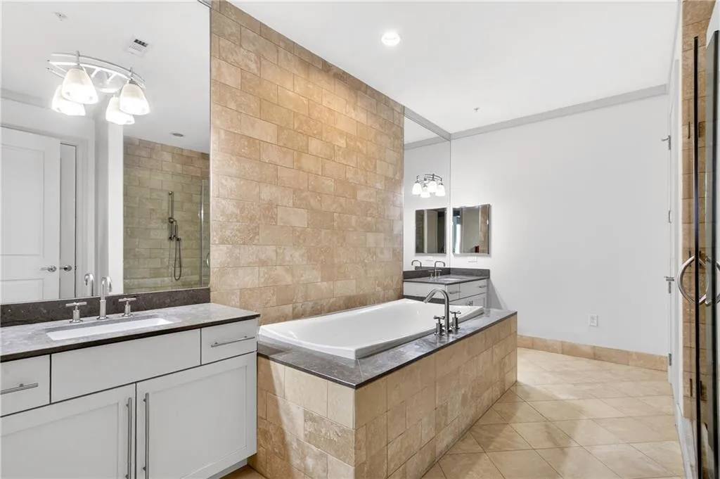 Full bathroom featuring a tile shower, tile walls, a garden tub, two vanities, and light tile patterned floors