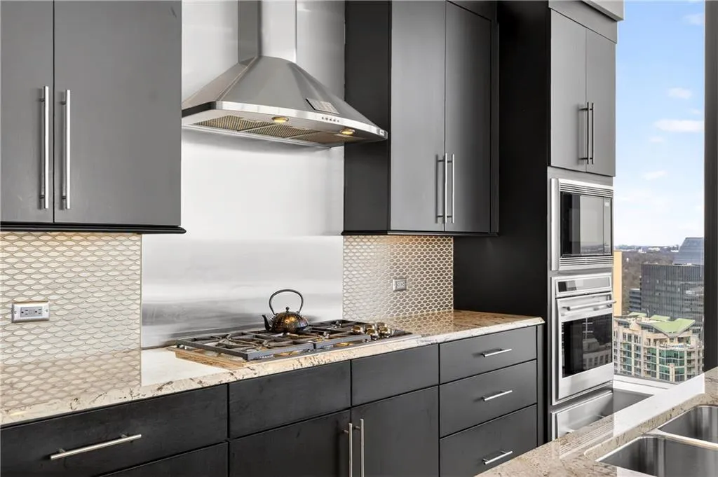 Kitchen with dark cabinetry, modern cabinets, light stone counters, built in appliances, and recessed lighting
