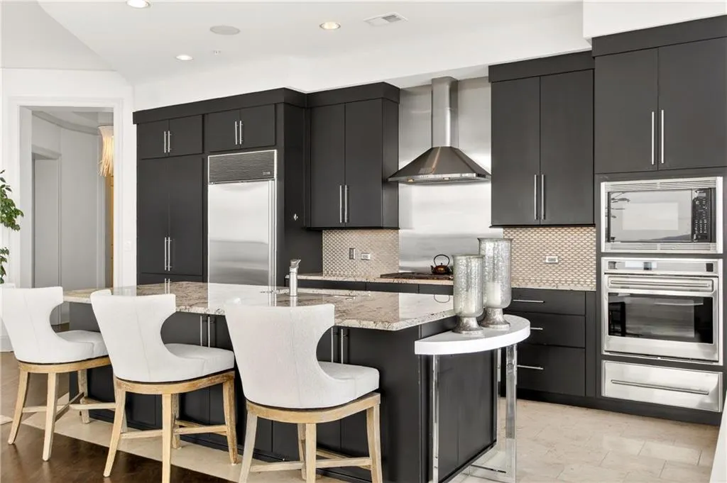 Kitchen with wall chimney exhaust hood, a city view, light stone counters, appliances with stainless steel finishes, and a warming drawer