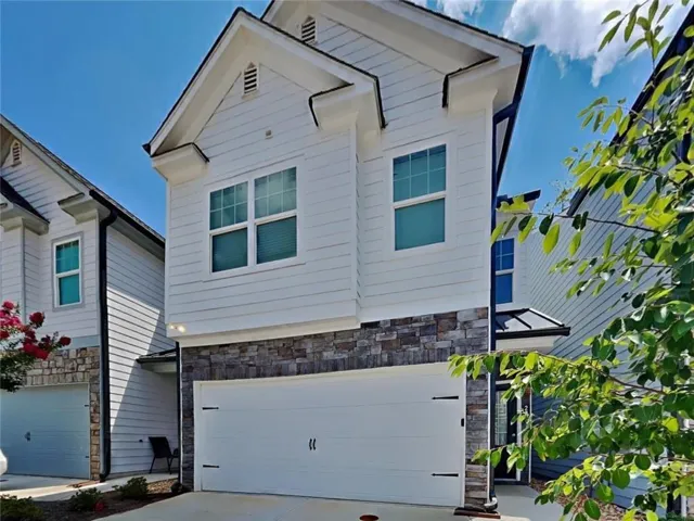 White siding exterior with stone accent, upper-level windows, attached garage, and prominent gables