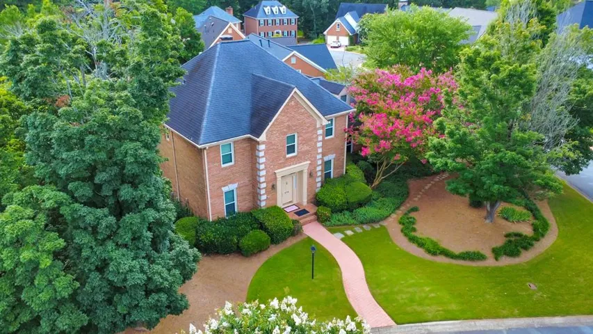 Traditional brick exterior featuring a dark-tiled roof, mature landscaping, a winding walkway, and vibrant pink flowering trees