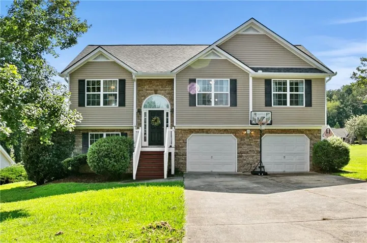 Split-level residence featuring a stone and siding exterior, arched transom entry, and a two-car garage