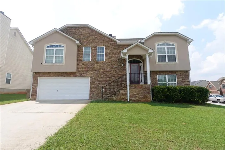 Exterior featuring a stone facade, stucco accents, arched windows, covered entry, and an attached two-car garage