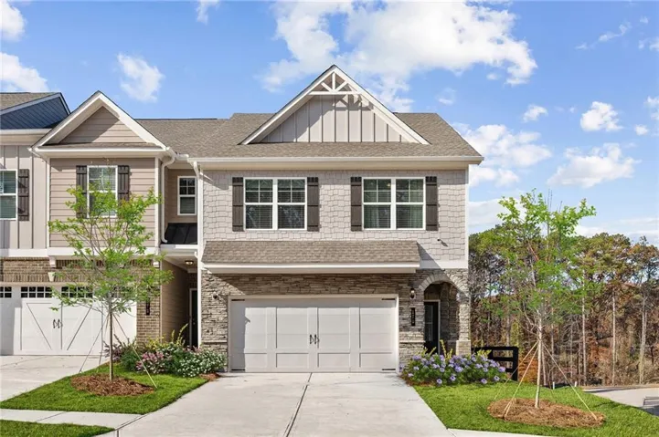 Contemporary townhome with a stone and shingle facade, featuring a prominent gable roof, two-car garage, and landscaped front yard