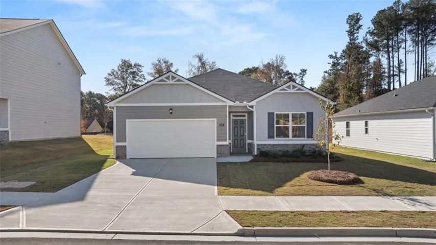 Single-story residence featuring light gray siding with stone-look accents, a covered entry, a white garage door, and a concrete driveway
