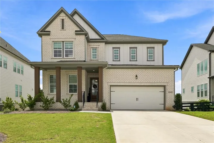 Brick and siding exterior featuring a two-car garage, covered entry with substantial columns, and mature landscaping