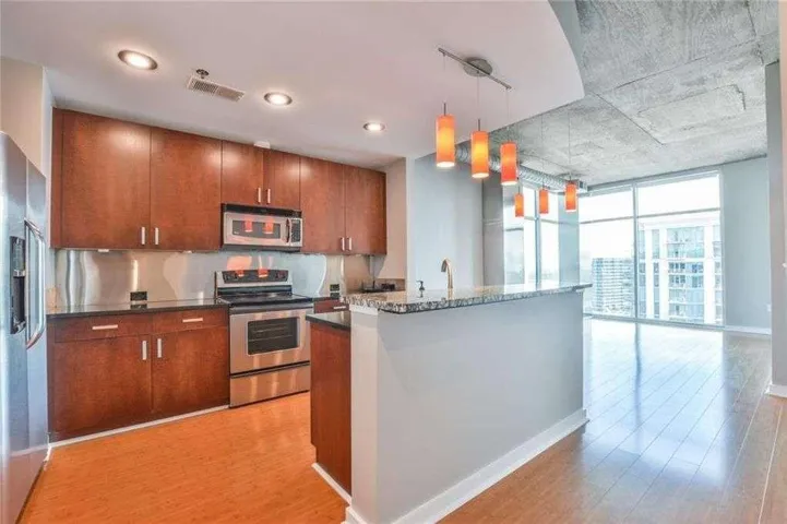 Kitchen featuring wood-finish flooring, dark stone countertops, wood cabinetry, and stainless steel appliances