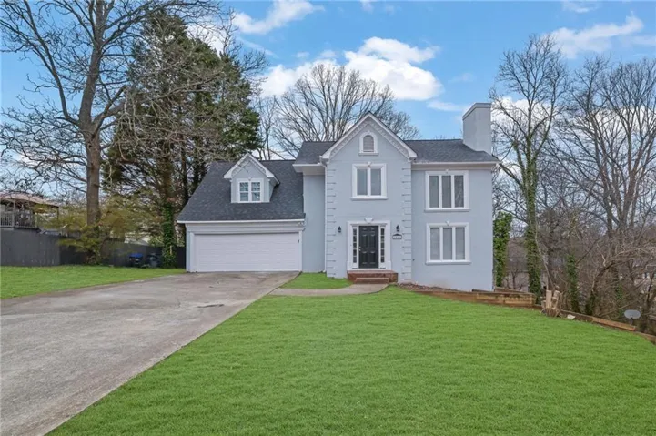 Light blue exterior featuring a dark front door, a two-car garage with an attached dormer, and multiple windows