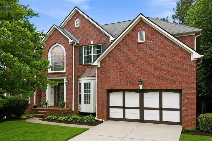 Brick exterior with architectural gables, arched window, bay window, and a two-car garage with decorative doors