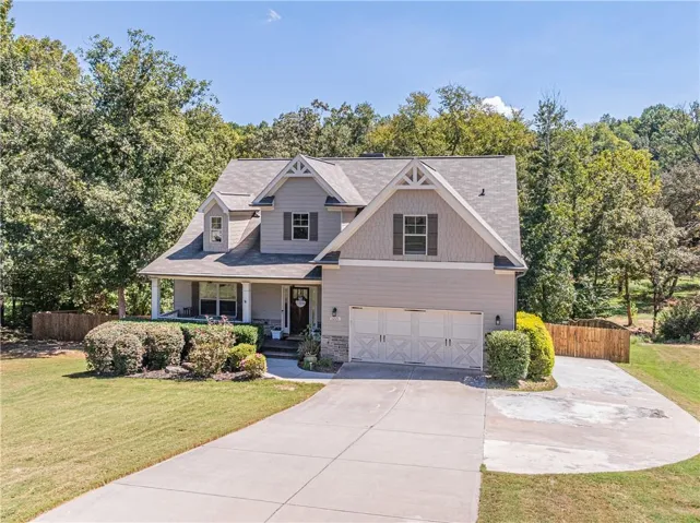 Gable roofline with dormer windows, stone accent siding, covered front porch, two-car garage with carriage-style doors, and concrete driveway