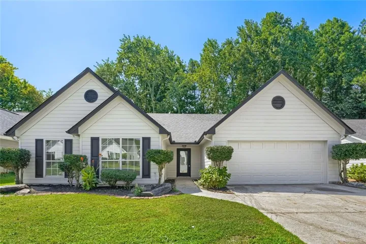 White siding exterior with black shutters, mature landscaping, an attached garage, and a concrete driveway