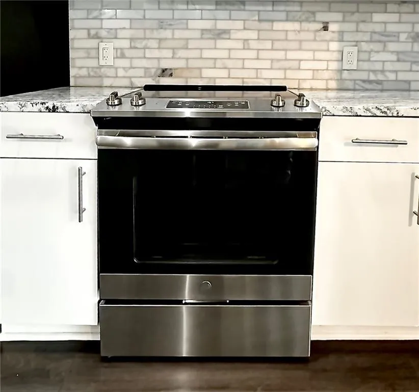 Kitchen view of electric range, tasteful backsplash, and light stone counters