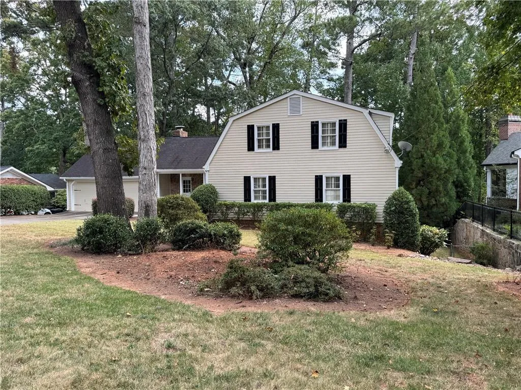 Dutch colonial with a gambrel roof, view of wooded area, an attached garage, and a chimney