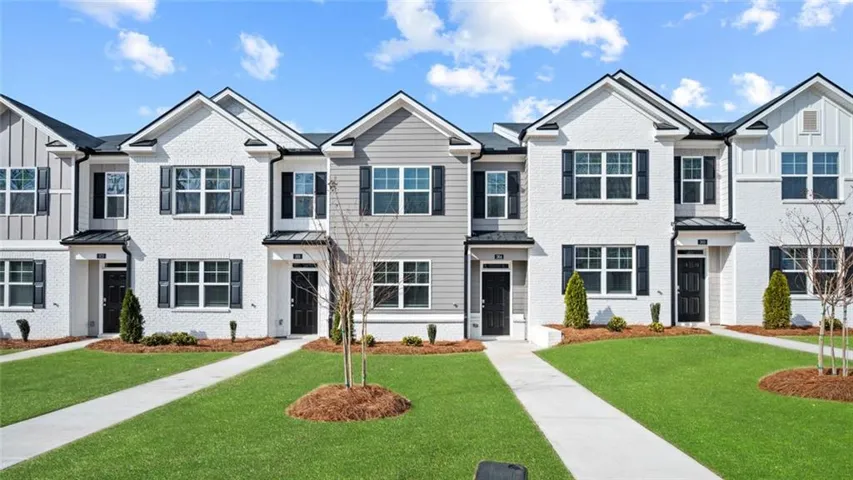 Two-story townhome with a white brick exterior, black shutters, and gabled roofline