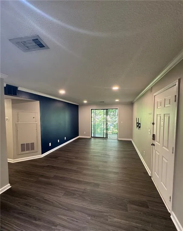Empty room featuring ornamental molding, a textured ceiling, dark wood-style flooring, and recessed lighting Empty room featuring ornamental molding, a textured ceiling, dark wood-style flooring, and recessed lighting